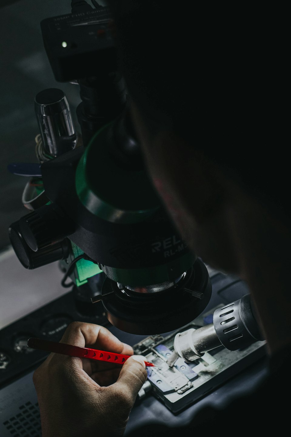 Technician using tweezers to repair a circuit board under a microscope.